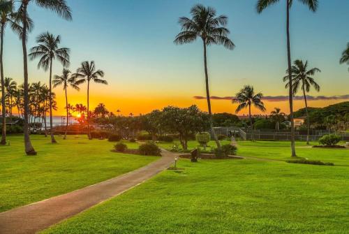 a sunset in a park with palm trees and a path at E111 Ground Floor Poolside Patio in Koloa