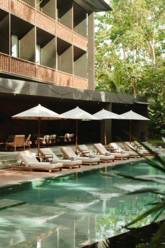 Una piscina con sillas y sombrillas al lado de un edificio. en Titik Dua, en Ubud