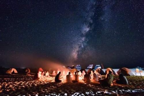 a group of people sitting around a bonfire on a beach at night at Abo Yusre Sfari in Bawiti