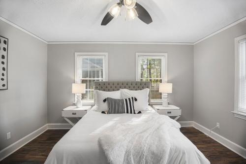 a white bedroom with a bed and two windows at Forest Hills Cottage in Augusta