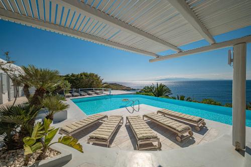 een zwembad met ligstoelen en uitzicht op de oceaan bij Sanarte Villas Mykonos in Mykonos-stad