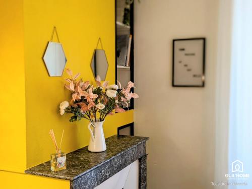 un vase de fleurs sur un comptoir avec un mur jaune dans l'établissement Ô plaisir des sens * Jardin * Parking * Plain-pied, à Orléans