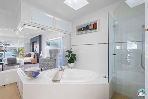baño blanco con bañera y ducha acristalada en Aircabin - Daleys Point - Waterfront Retreat House en Daleys Point