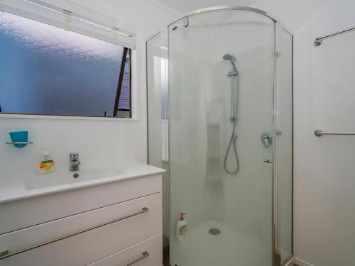 a white bathroom with a shower and a sink at Beachfront Beauty - Whangamata Beachfront Home in Whangamata