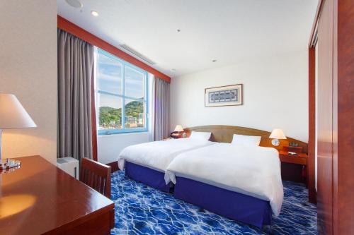a hotel room with a bed and a desk and a window at Premier Hotel Mojiko in Kitakyushu
