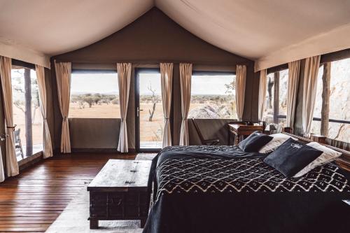 ein Schlafzimmer mit einem Bett in einem Zimmer mit Fenstern in der Unterkunft Ohorongo Tented Camp in Outjo