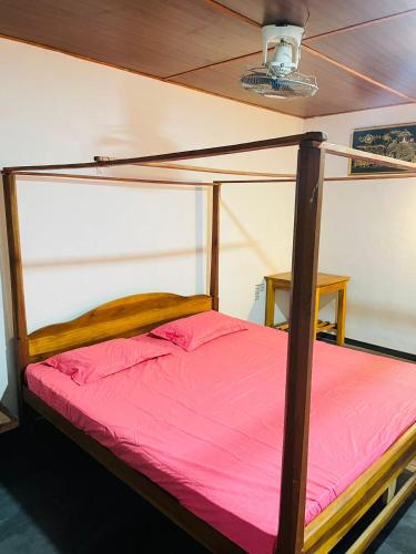 a bed with a wooden frame and pink sheets at Rivinu Place Arugambay in Arugam Bay