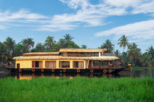 a large yellow boat on a river with palm trees at IndraprasthamLakeCruise in Alleppey