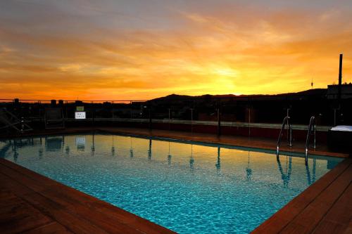 a large swimming pool with a sunset in the background at Hotel 1898 in Barcelona