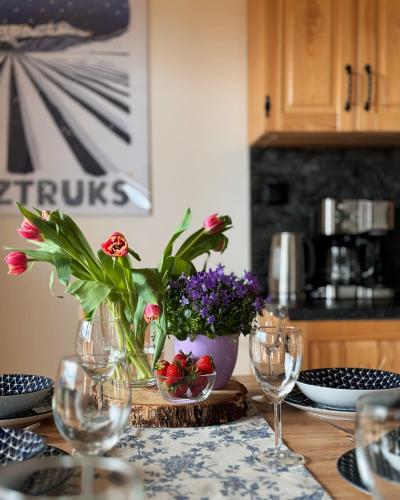 a table with glasses and a vase with flowers on it at Apartamenty na Soszowie, Wisła - widokowe miejsce z Balią & Prywatną Sauną, obok stoku narciarskiego i Bike Parku, dla max 16 osób in Wisła