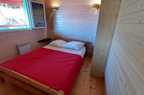 a small bed in a small room with a red blanket at maison en bois in Lacapelle-Viescamp