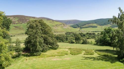 a green field with trees and hills in the background at Mossfennan House & Annexe in Drummelzier