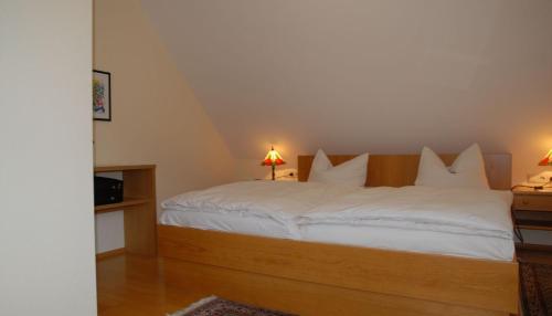 um quarto com uma cama com lençóis brancos e 2 candeeiros em Hotel Garni Grottental em Meßstetten