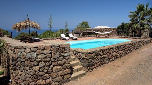 una pared de piedra alrededor de una piscina en un complejo en Lighted Pool, Barbecue & Sea View - Authentic "Dammusi" en Pantelleria