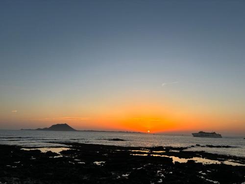 una puesta de sol sobre el océano con un crucero en la distancia en Dunas Club - Hotel & Apartamentos, en Corralejo