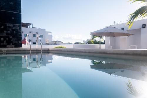 a swimming pool with an umbrella next to a building at Arkana 9 Suites by Grupo Amber in Playa del Carmen