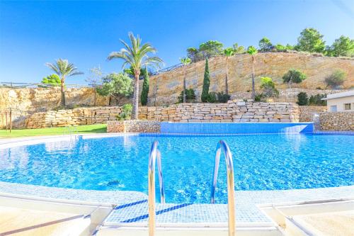 una piscina con palmeras y una pared de piedra en Highrise apartment with private terrace & sea views - 34th floor en Benidorm