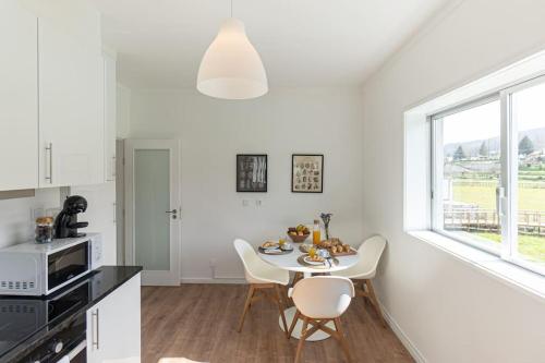 a white kitchen with a table and white chairs at Casa da Ecovia in Arouca