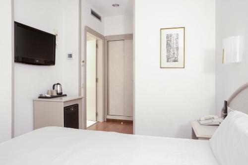 a white bedroom with a bed and a tv on the wall at Hotel Lleó in Barcelona