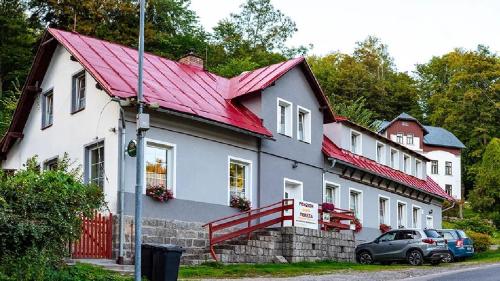 a white house with a red roof with cars parked in front at Penzion Tereza in Janov nad Nisou