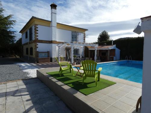 uma villa com piscina e 2 cadeiras verdes em Villa Los Corralillos de Pepa em Padul