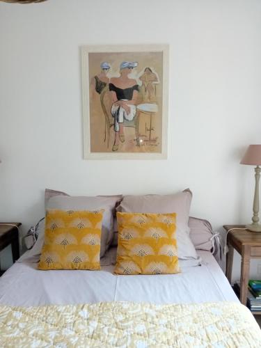 Una cama con almohadas amarillas y una pintura encima. en Chambre d hotes de charme, en Vernon