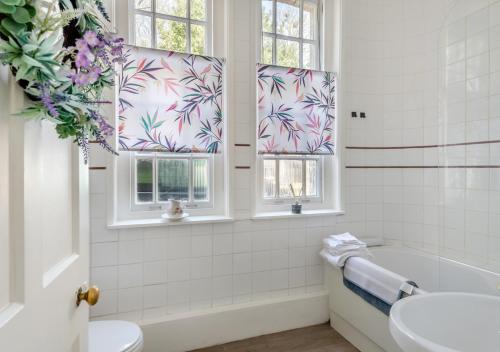 a bathroom with a tub and a sink and two windows at The Lake House - Crimplesham Hall in Stradsett