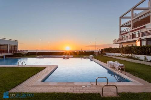 a large swimming pool with a sunset in the background at Gaia Beach & Pool Residence - Porto South Seashore in Vila Nova de Gaia