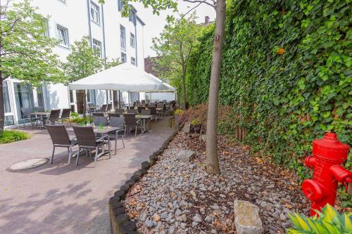 a red fire hydrant next to a hedge with tables and chairs at Dorint Hotel Würzburg in Würzburg