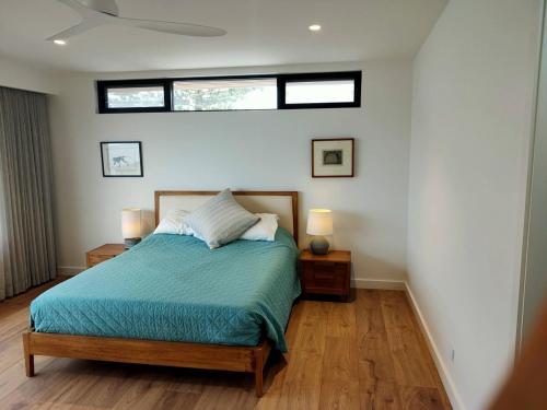 a bedroom with a bed with a blue comforter and two windows at Chic Coastal Retreat Prime Setting in Curl Curl