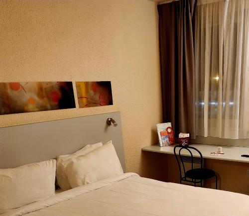 a bedroom with a bed and a desk and a window at The Originals City, Hôtel Le Forum, Strasbourg Nord in Schiltigheim