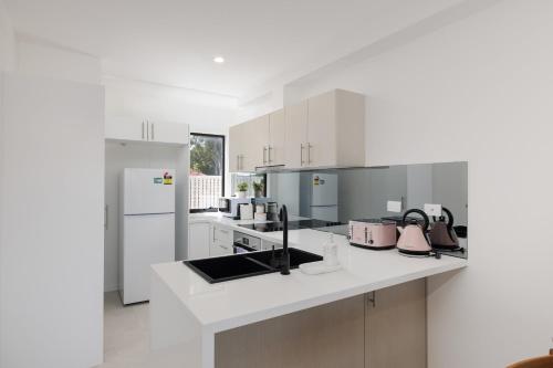 a white kitchen with a sink and a refrigerator at Netflix Brand new 4BR Fast NBN AC Free Parking in Gold Coast
