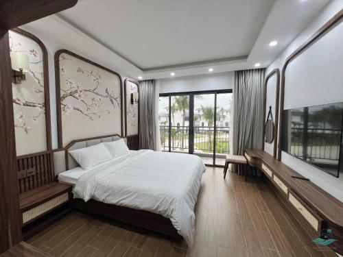 a bedroom with a bed with white sheets and windows at Rosa Villa - Sonasea Vân Đồn in Cái Rồng