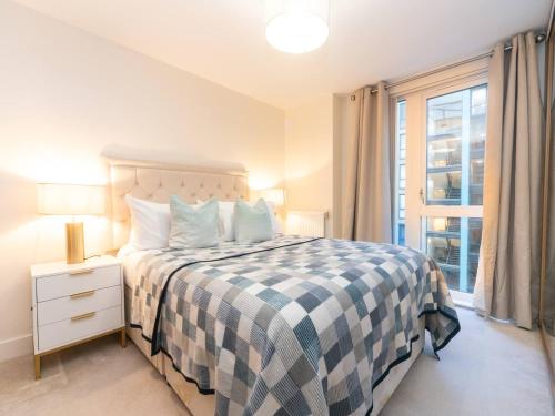 ein Schlafzimmer mit einem Bett mit einer karierten Decke und einem Fenster in der Unterkunft Pass the Keys Modern 2 bedroom and 2 Bath Apartment in London in Edgware