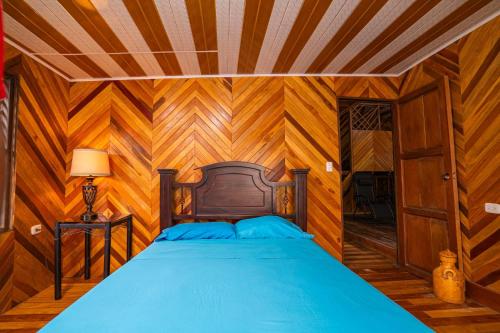 ein Schlafzimmer mit einem blauen Bett in einem Zimmer mit Holzwänden in der Unterkunft Casa Almendro Playa Panamá in Panamá