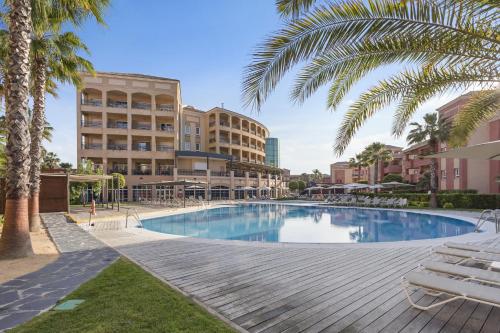 a swimming pool with palm trees and buildings at AMA Residences Andalucia in Islantilla