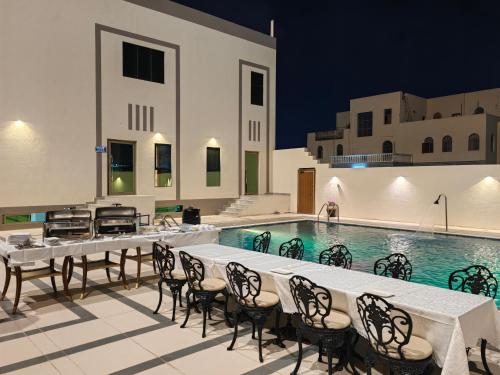 ALYA Hotel في بركاء: منطقة لتناول الطعام بجانب حمام السباحة مع طاولات وكراسي بجوار مبنى