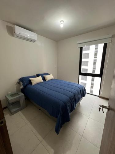 Schlafzimmer mit einem Bett mit blauer Bettwäsche und einem Fenster in der Unterkunft Departamento frente al TSM in Torreón