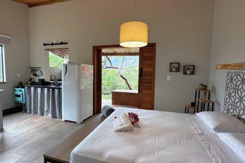 a bedroom with a white bed and a kitchen with a refrigerator at Cabanas da Mata - Cabana Flamboyant - Casa Branca in Brumadinho