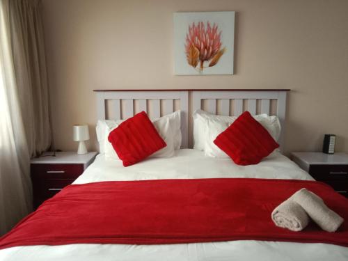 een bed met rode kussens en een rode deken bij Edladleni Guesthouse Quigney in East London