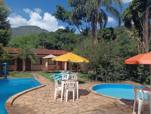 un patio con sillas y una sombrilla junto a la piscina en Pousada Maravilhas da Serra en Moeda