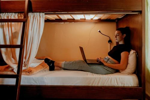 una mujer sentada en una litera con un ordenador portátil en Berat Backpackers Hostel en Berat