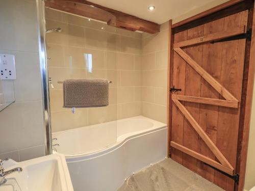 a bathroom with a tub and a shower with a door at Boskins in Sedbergh