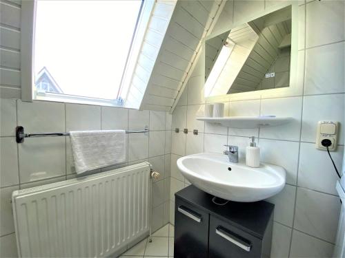 ein weißes Badezimmer mit Waschbecken und Spiegel in der Unterkunft Haus Waldesblick An der Rennweide 26a 75 qm in Dangast