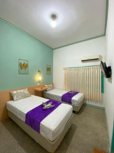2 Betten in einem Hotelzimmer mit violetter Bettwäsche in der Unterkunft The Sri Rejeki Hotel in Blitar