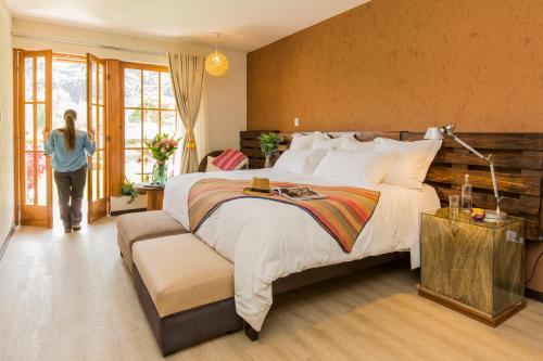 une femme debout dans une chambre avec un grand lit dans l'établissement Lamay Lodge by Mountain Lodges of Peru, à Cusco