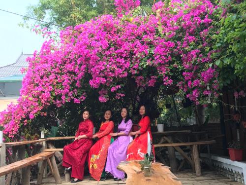 Tres mujeres sentadas bajo un árbol con flores rosas en Homestay Minh Ngọc en Diện Biên Phủ