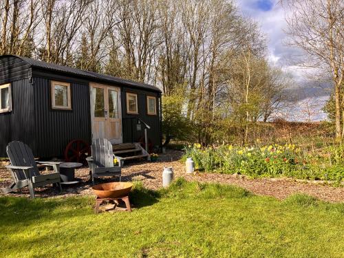 a black tiny house in a garden with flowers at Archie the shepherd’s hut in Penruddock