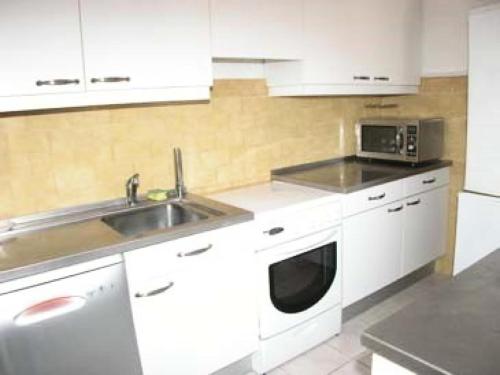een keuken met witte kasten, een wastafel en een magnetron bij Résidence LES PATIOS 1 - Maisons & Villas pour 6 Personnes 84 in Port Leucate