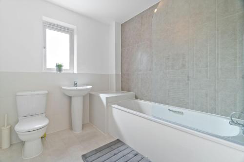 a white bathroom with a toilet and a tub and a sink at Cosy 3 Bedroom Spacious house. in Romford